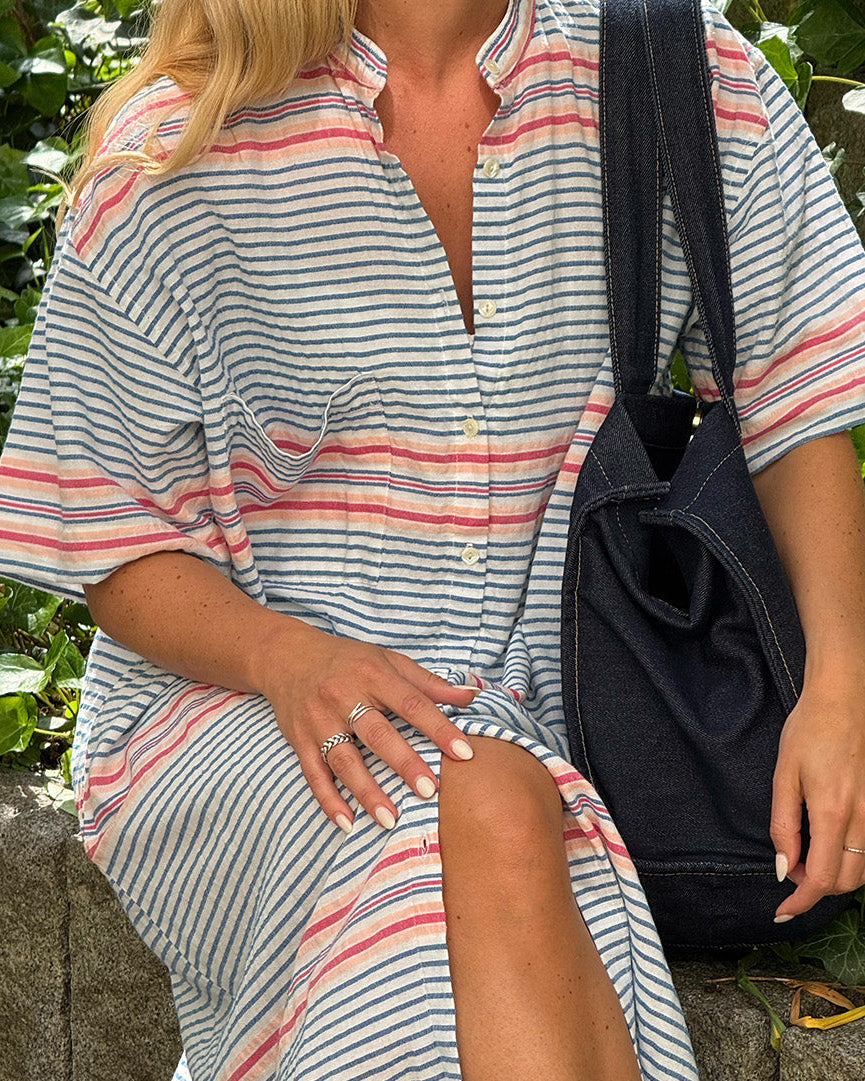Person wearing a striped dress with a black bag against a green leafy background